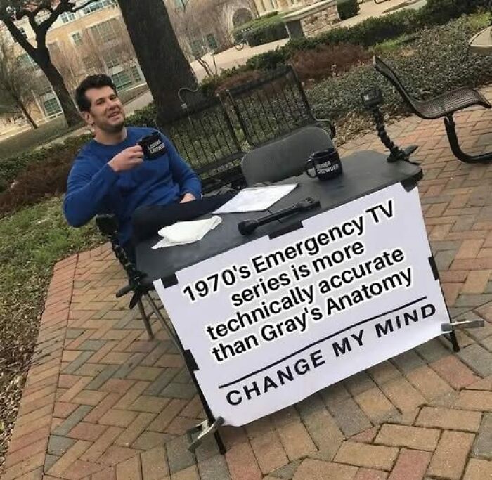 Person at a table holding a mug with a sign about 1970s emergency TV accuracy, relevant to EMT and paramedic memes.