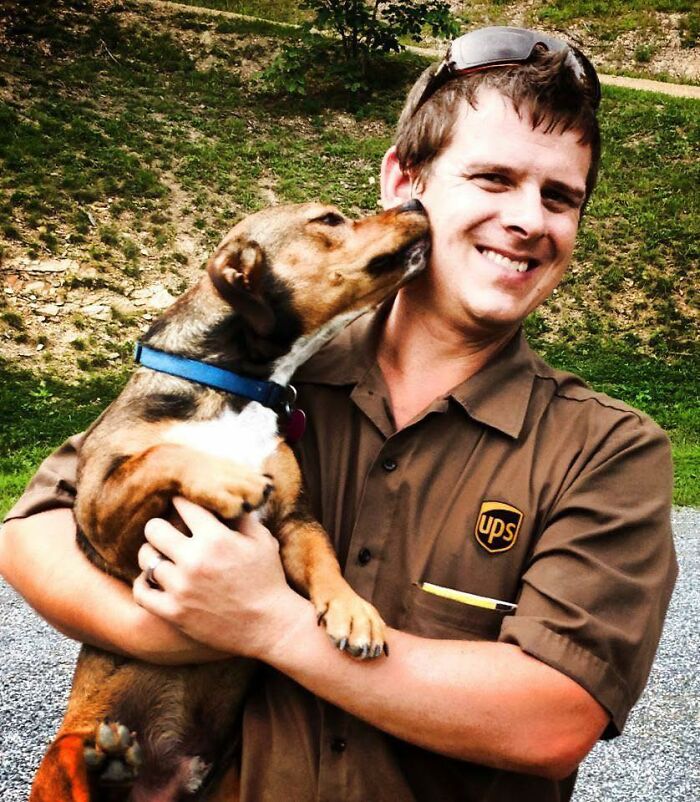 UPS driver smiling and holding an adorable dog giving a kiss outdoors during a delivery visit with pets.