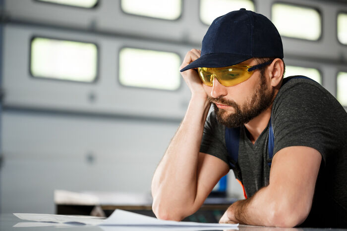 Man in a cap and yellow glasses reflecting deeply while looking at papers, symbolizing life-changing sentences tattooed on hearts.