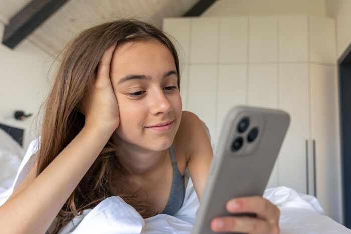 Young woman relaxing in bed, smiling while looking at her phone, illustrating relationship dealbreakers revealed by women.