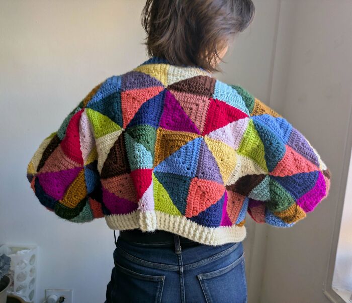 Person wearing a colorful crocheted jacket featuring geometric patterns and a variety of vibrant yarn colors.