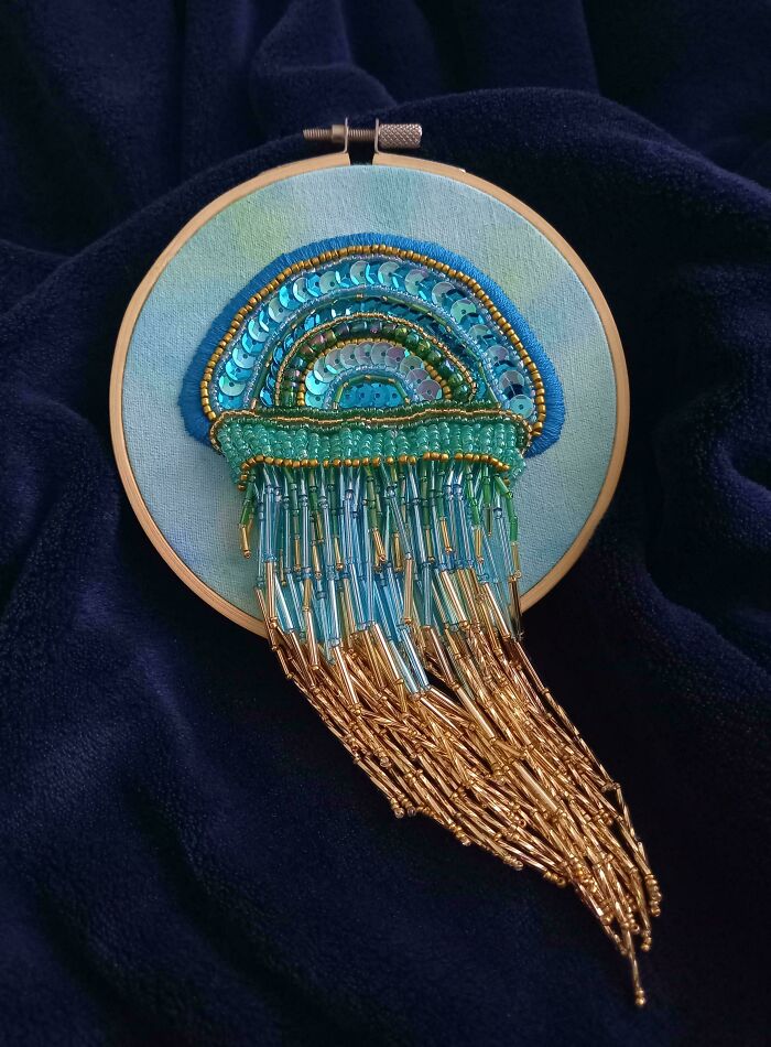 An exquisite embroidery creation resembling a jellyfish, adorned with blue and gold sequins and beads, framed in a hoop.