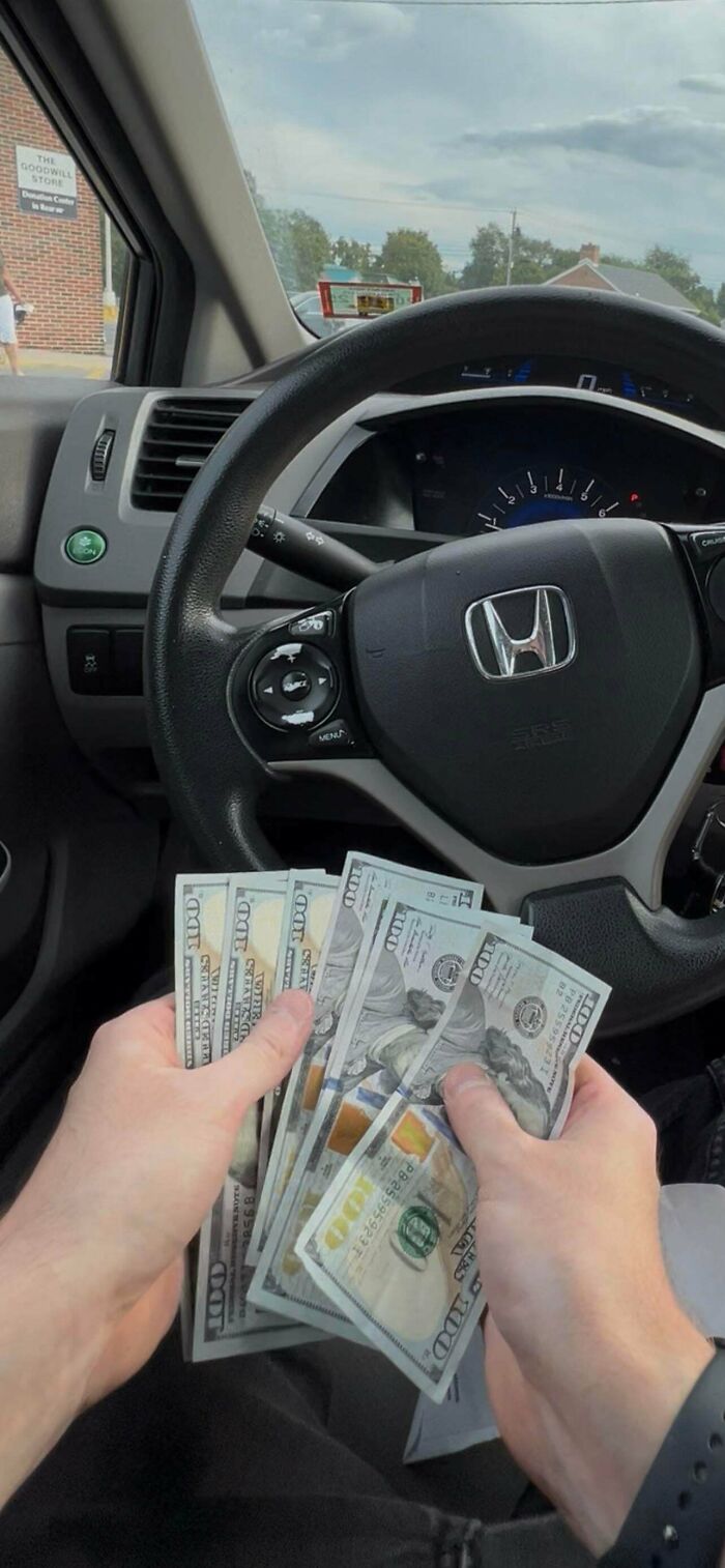 Person holding cash inside a car parked outside a thrift store, showcasing thrift store finds like stumbling upon treasure.
