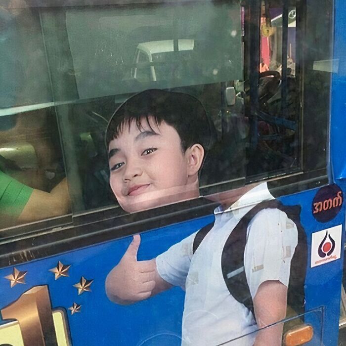 Boy giving thumbs up on a bus advertisement, blending awkwardly with the reflection for an advertising placement fail.