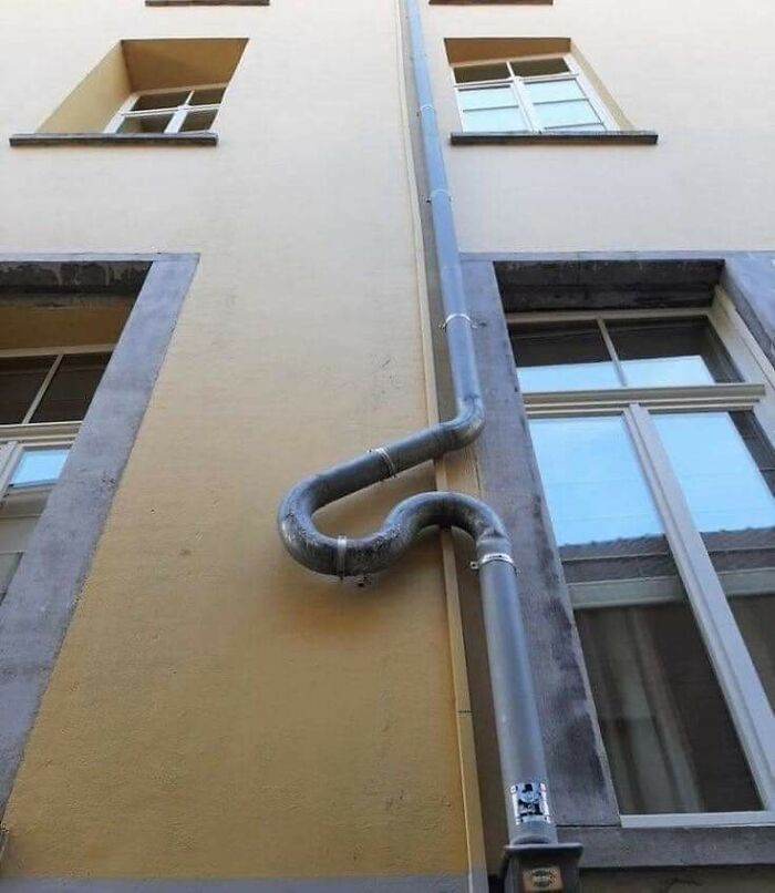 Poorly installed drainpipe on building exterior with awkward bends, example of hilariously bad jobs done by someone just getting it over with.