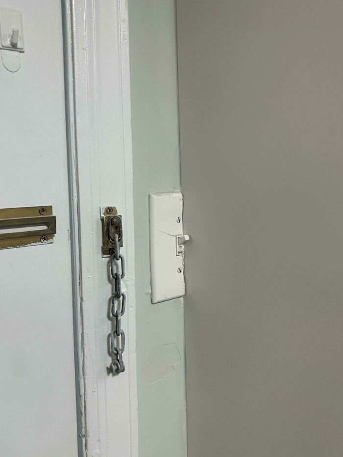 A poorly installed door chain and misaligned light switch showcasing hilariously bad jobs done carelessly.