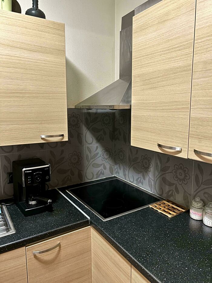 Kitchen corner with wooden cabinets and a black countertop featuring a poorly installed stovetop showing bad jobs.