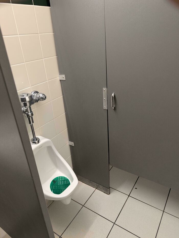 Public restroom with a poorly installed stall door blocking access to the urinal, showing hilariously bad job quality.