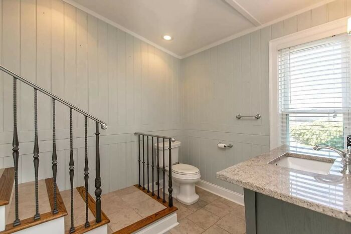 Bathroom with poorly placed toilet next to stair railing, showcasing hilariously bad jobs done just to get it over with.