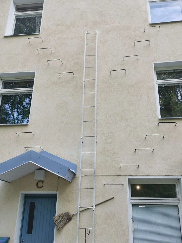 Poorly installed ladder with uneven steps and a broom stuck between the ladder and the building wall, showing bad job quality.