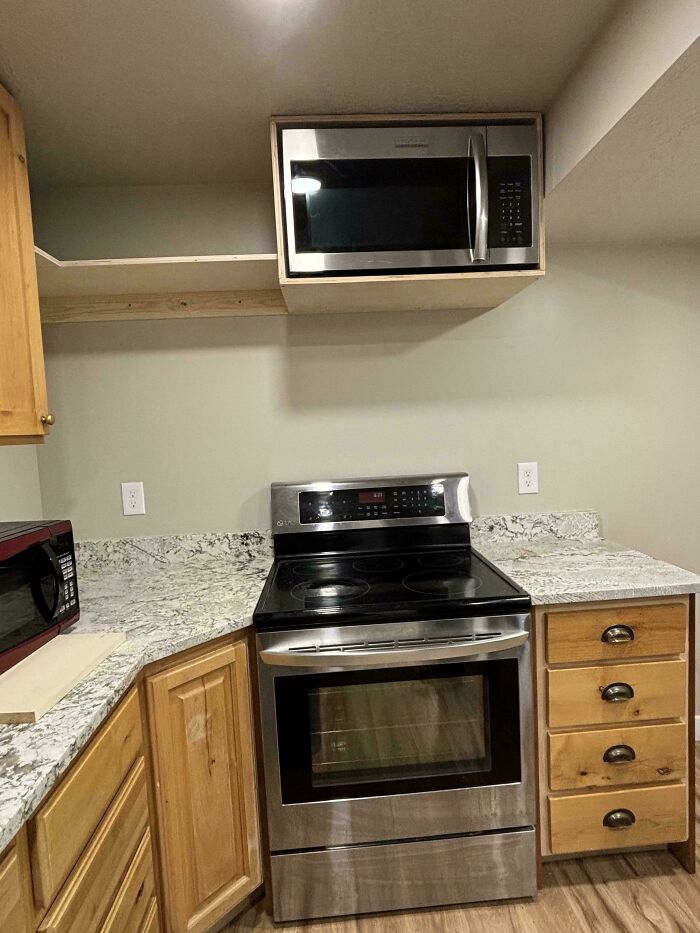Microwave poorly installed in kitchen cabinet space above stove, showing a hilariously bad job done carelessly.