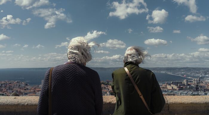 Two elderly individuals with white hair stand overlooking a cityscape in a striking street photo that feels like movie stills.