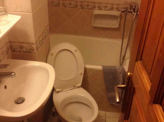 Bathroom with poorly installed toilet seat and awkwardly placed towel in a small, tiled space showing a bad job done carelessly.