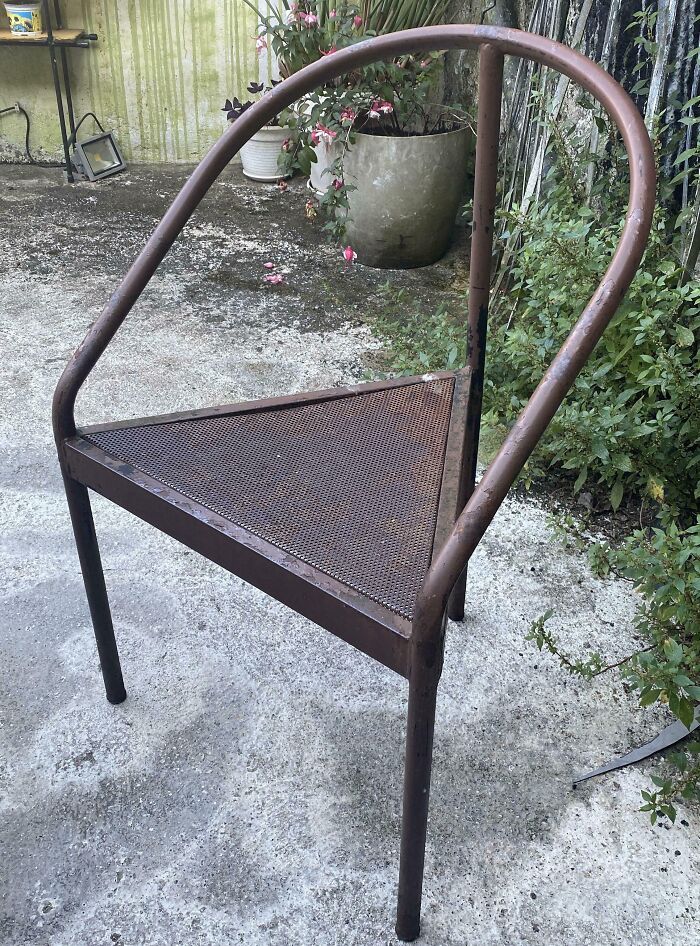 Rusty metal chair with poorly done triangular seat showing hilariously bad jobs and quick fixes outdoors.