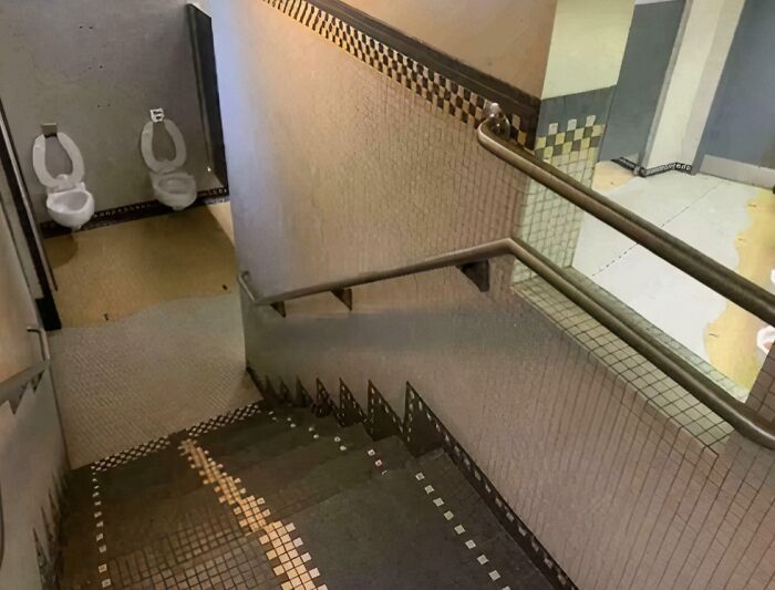 Stairs leading down to a restroom with two toilets installed unusually close together, showing a hilariously bad job.
