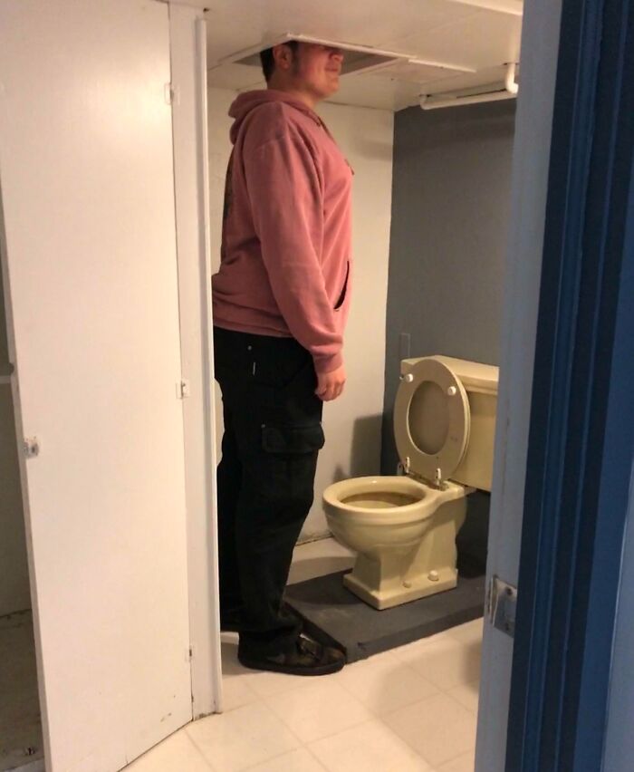 Person standing in a bathroom with a low ceiling above a toilet, illustrating hilariously bad jobs done quickly.