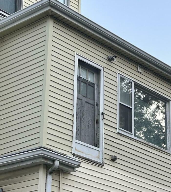 Poorly installed door on second story of house with no stairs, showing a bad job done without care.