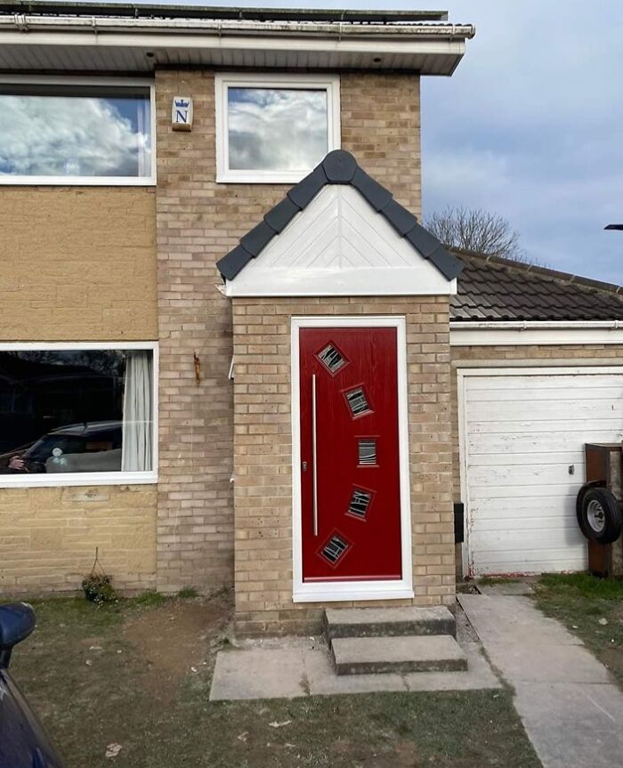 Red front door with crooked, misaligned windows installed on a suburban house, showing a hilariously bad job.