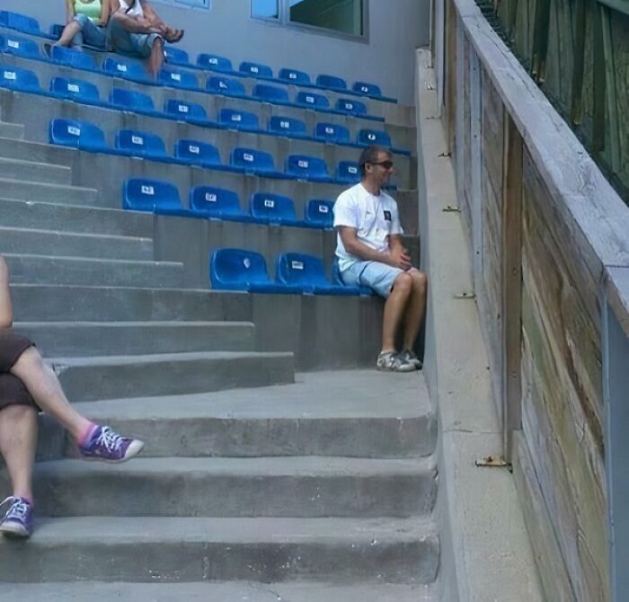 Man awkwardly sitting on a misplaced stadium seat in empty bleachers, illustrating hilariously bad jobs done carelessly.