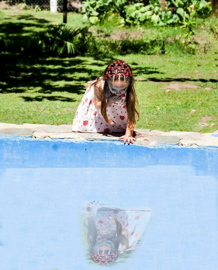 Young girl with braided hair leaning over pool edge with distorted reflection, showcasing Photoshop fails in editing images outdoors.