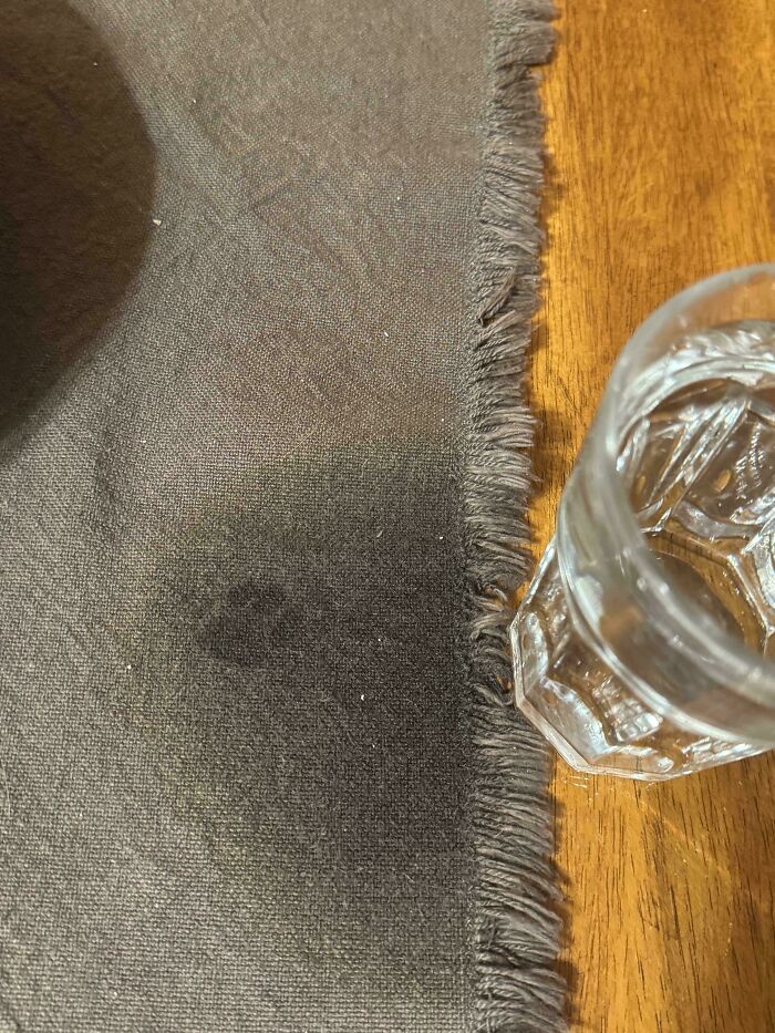 Faint cat paw print on a dark fabric next to a clear glass on a wooden table showing cute cat paw prints.