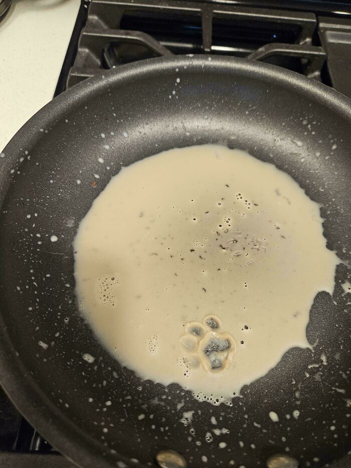 Pancake batter cooking in a pan with a clear cute cat paw print shape in the batter near the edge.