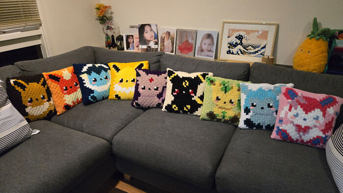 Crocheted pixel art cushions featuring colorful characters displayed on a gray sectional sofa, showcasing creative crocheting projects.