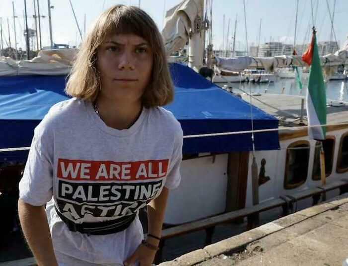 A person with an unfortunate haircut, standing in a harbor with boats in the background. Another one of the worst haircuts.
