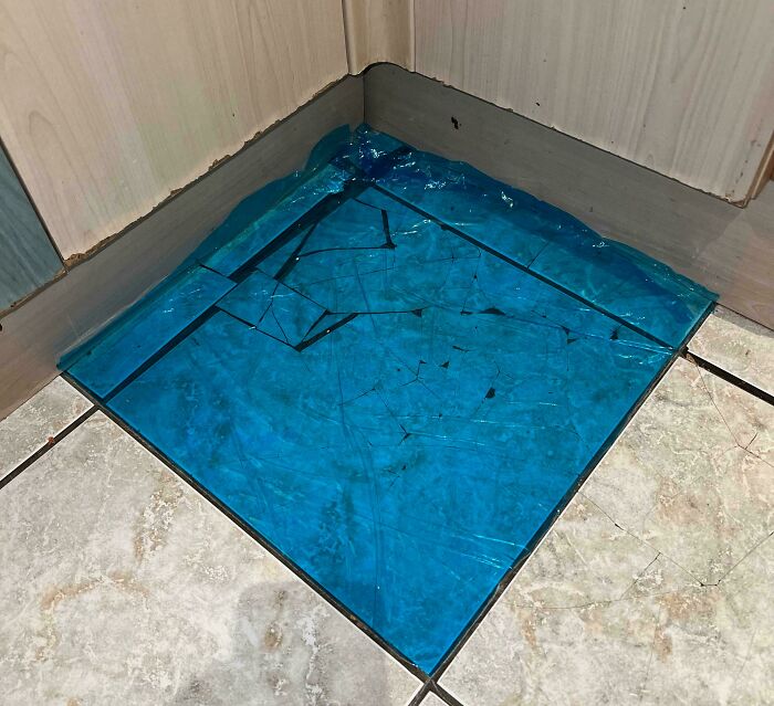 Broken blue floor tile with water pooling in the corner, showing poor maintenance by landlords in rental property.