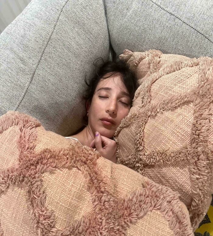 Young woman sleeping peacefully on a couch surrounded by textured pillows, capturing a beautiful accidental renaissance moment.