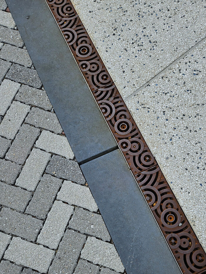 Decorative metal drain cover with circular patterns between textured concrete and brick pavement showcasing smart design.