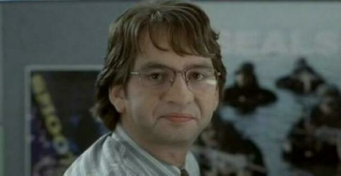 Man with glasses and medium-length hair smiling, evoking 90s posts and nostalgic memories in an indoor setting.