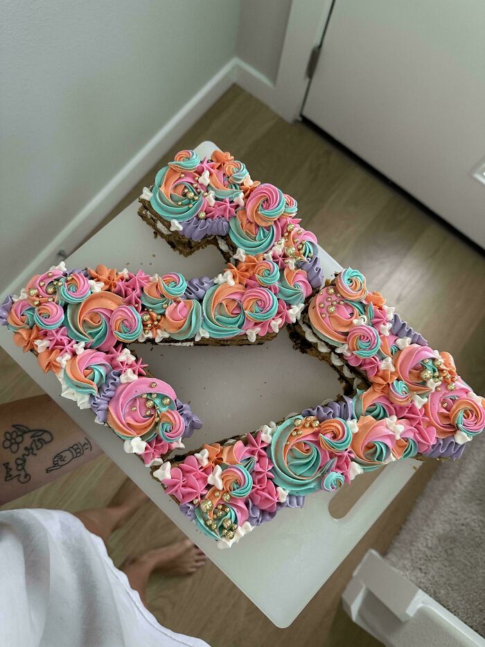 Colorful baked goods shaped like an Instagram logo decorated with intricate pastel swirls and gold sprinkles on a white board.
