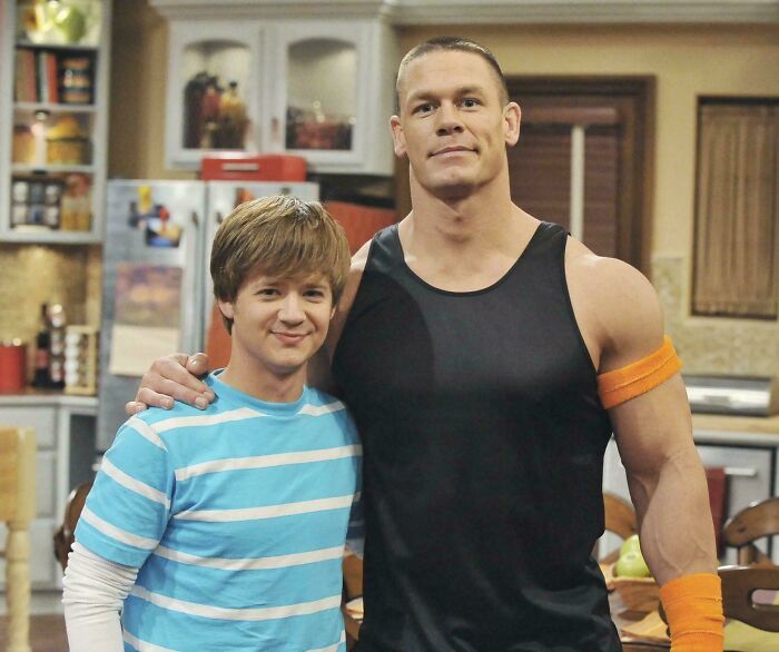 Actor John Cena and a young co-star posing in a kitchen setting, featured in bad movie details discussion group.