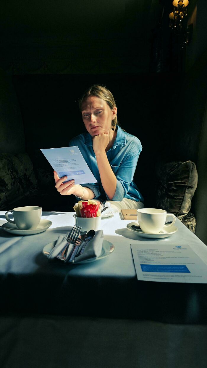 Woman in soft natural light reading a menu at a table set with cups and cutlery in an accidental Renaissance photo style.