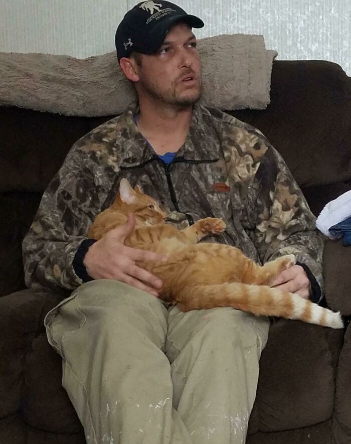 Man in camouflage jacket holding an orange cat on his lap, showing dads who said no pets becoming total softies.