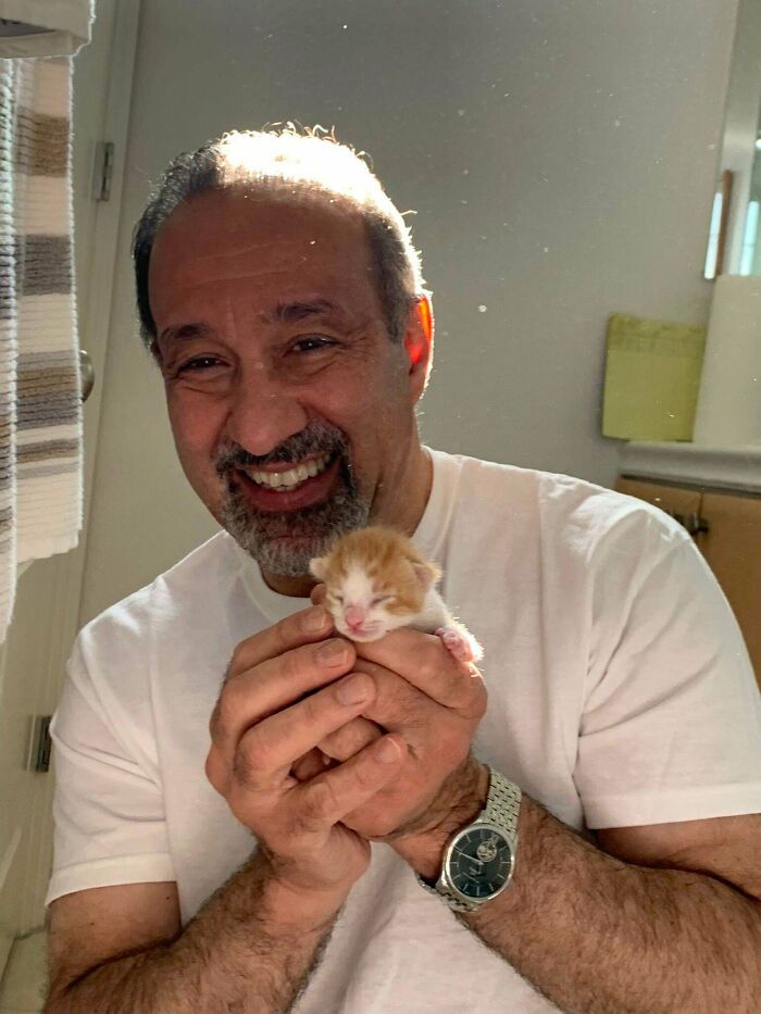 Smiling dad holding a tiny newborn kitten indoors, showing the soft side of dads who said no pets at first.
