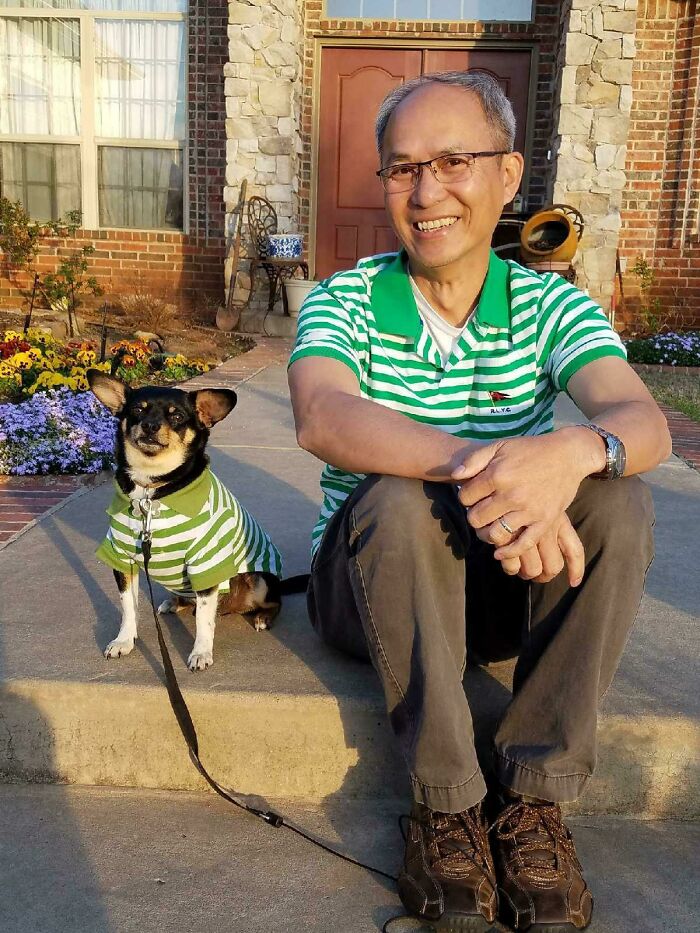 Man and dog wearing matching green striped shirts sitting on a sidewalk, showing dads who said no pets becoming softies.