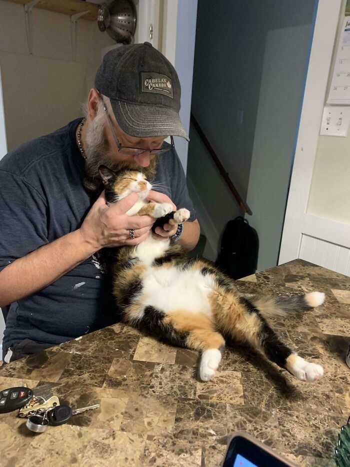 Man showing affection to a calico cat on a kitchen table, highlighting dads who became softies despite no pets rule.