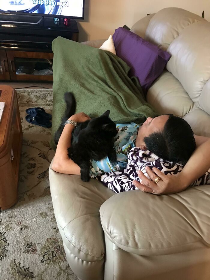Man relaxing on couch with black cat resting on his chest, showing dads who said no pets becoming total softies.