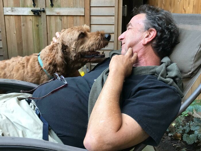Man relaxing in a chair sharing a happy moment with his dog, showing dads who said no pets becoming softies.