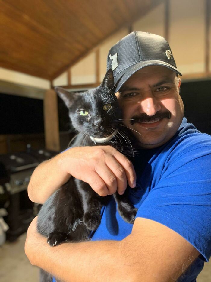 Man smiling and holding a black cat in a warm embrace, showing dads who said no pets becoming total softies.