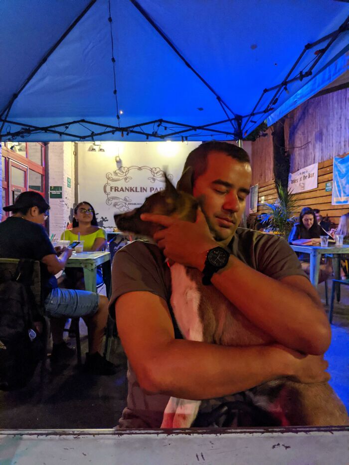 Man hugging dog warmly under blue tent at outdoor café, showing dads who said no pets becoming softies.
