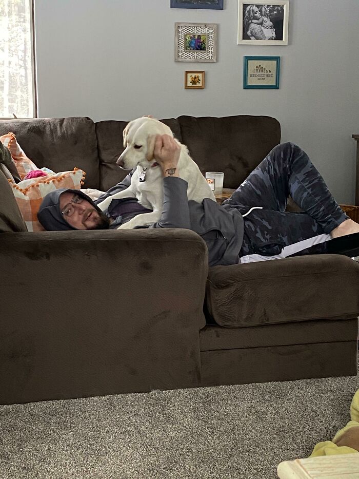 Man lying on a couch with a white dog on his chest, showing dads who said no pets but became softies.