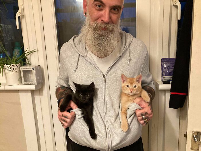 Man holding two kittens inside his hoodie, showing the soft side of dads who said no pets initially