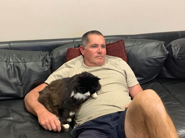 Man relaxing on a couch with a black and white cat, showing dads who said no pets becoming total softies.