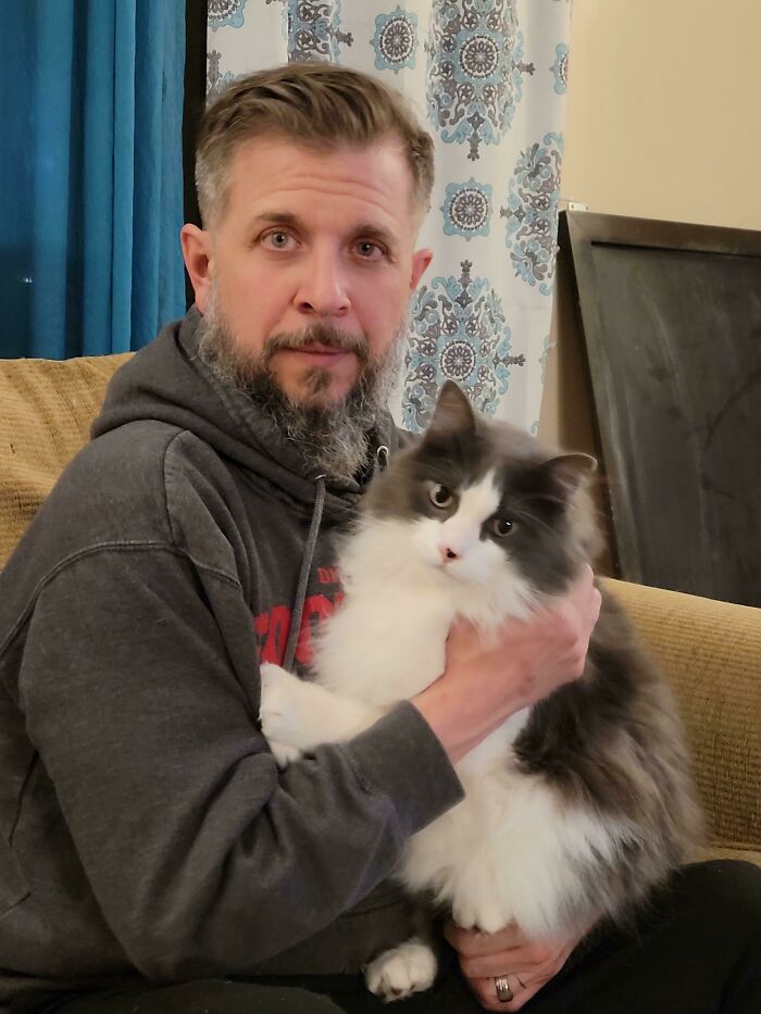 Dad holding a fluffy gray and white cat, showing a soft and caring moment with pet in a cozy living room.