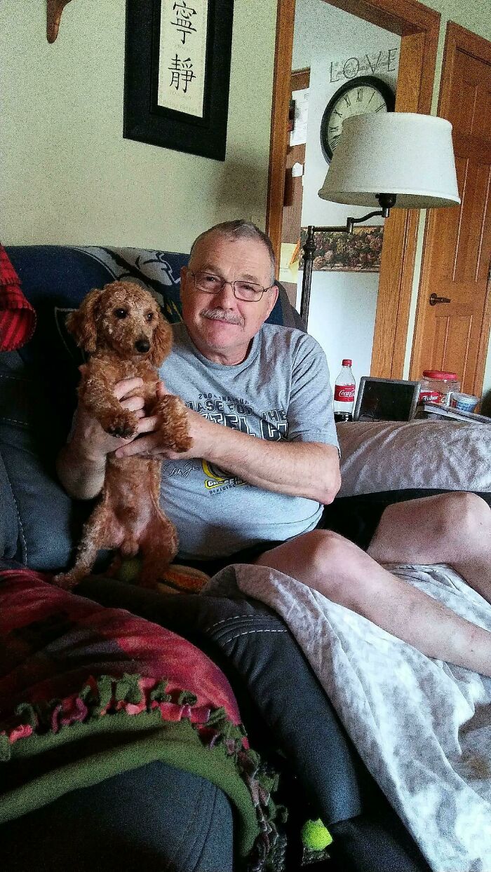 Man holding a small brown dog on a couch, illustrating dads who said no pets and became total softies.