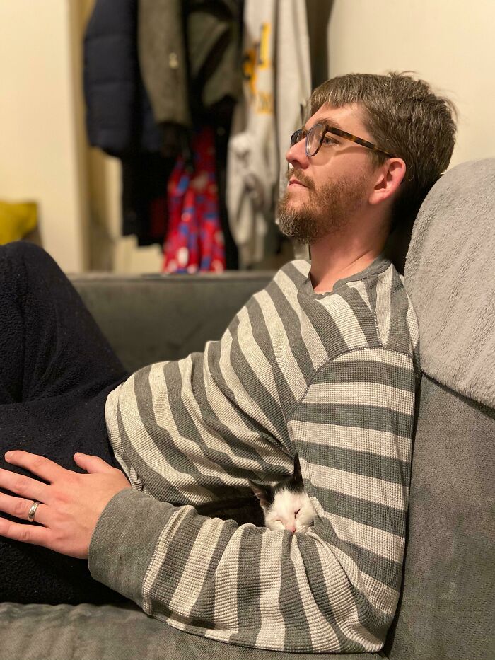 Man wearing glasses and striped shirt relaxing on couch with small kitten, a heartwarming moment of dads becoming total softies with pets.
