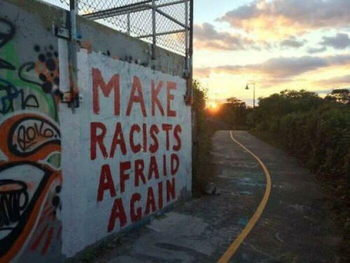 Graffiti vandalizing public property with a political message at sunset along an empty paved path.